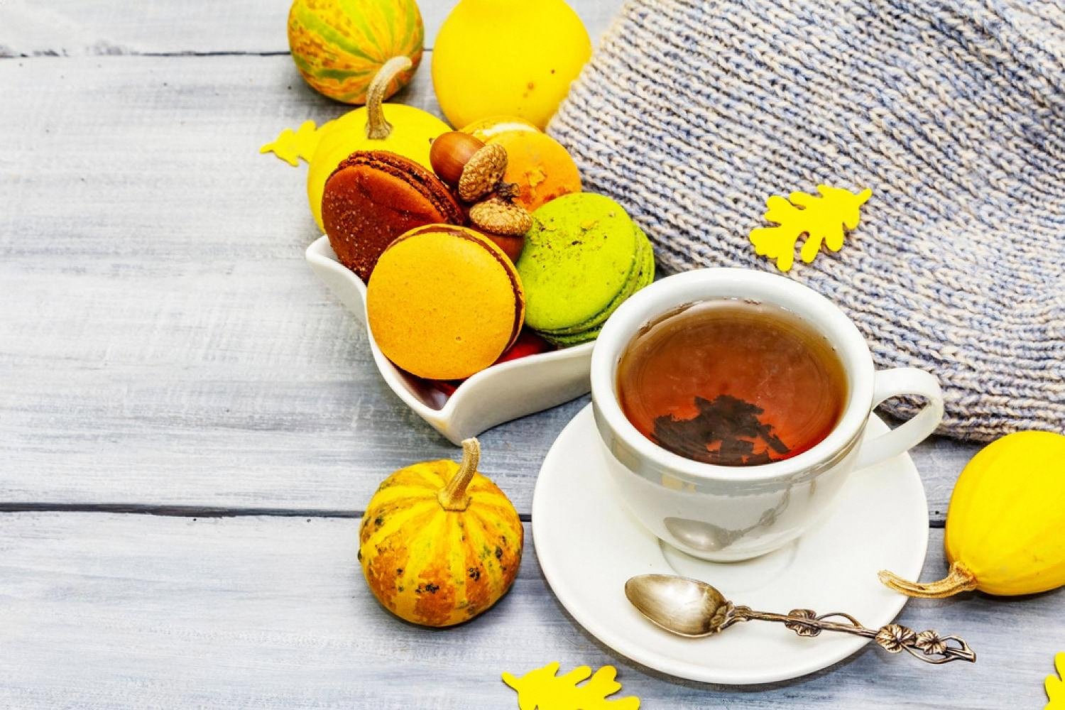 Cup of freshly brewed black tea with visible leaves next to autumn macarons on a wooden table