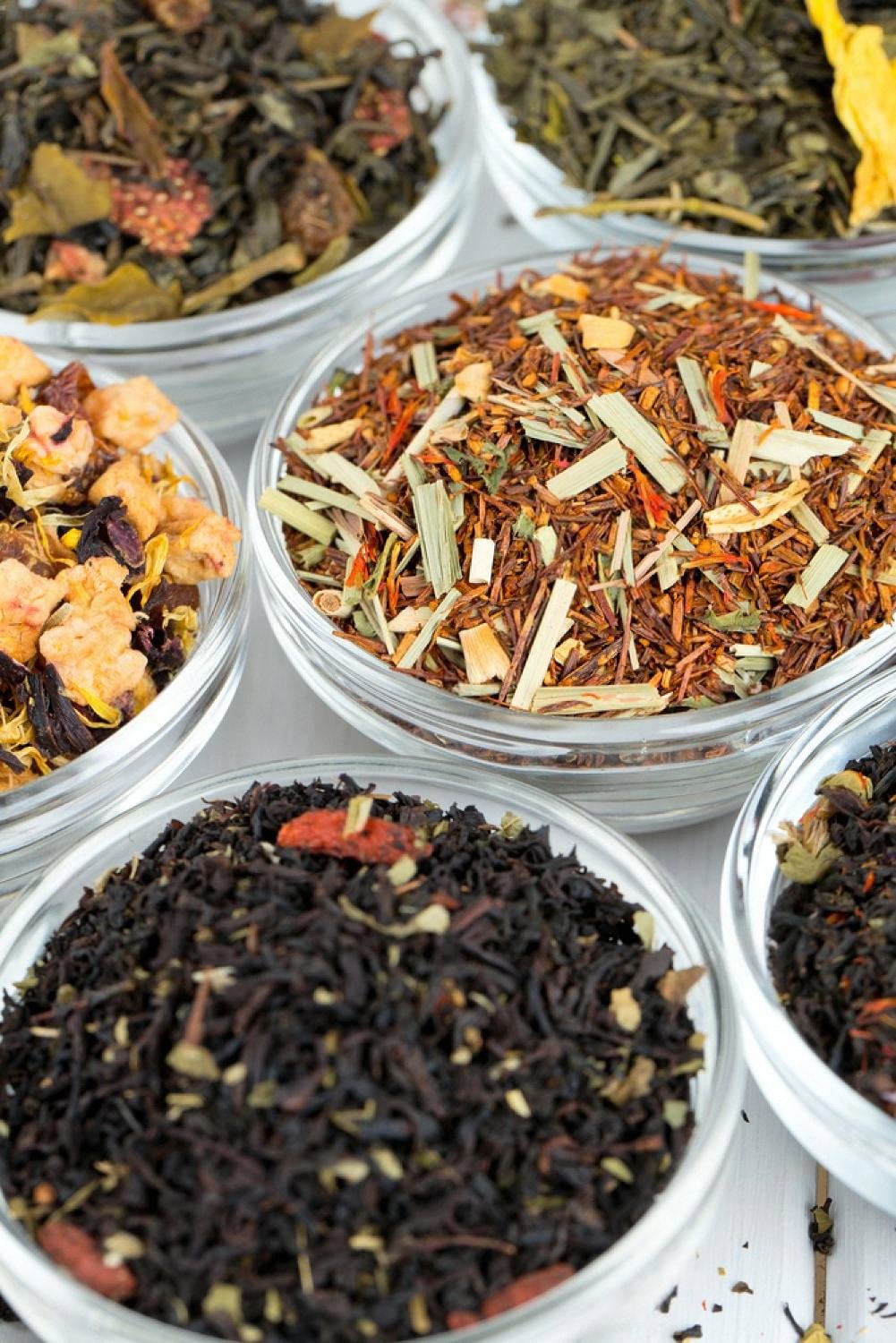 Bowls of loose-leaf tea varieties including black, green, rooibos and fruit blends on a shop counter